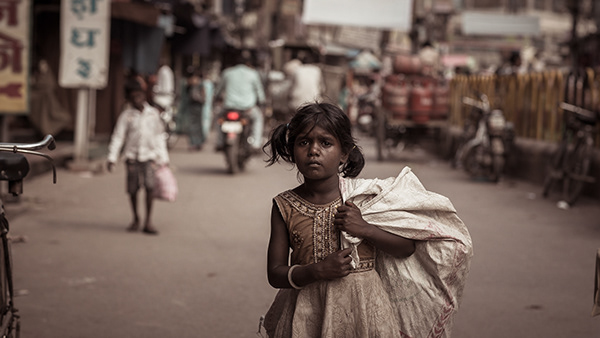 Child carrying a large white sack along a street