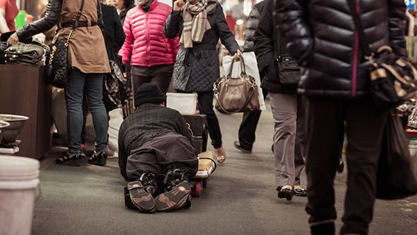 Person bowing on the pavement among passing pedestrians