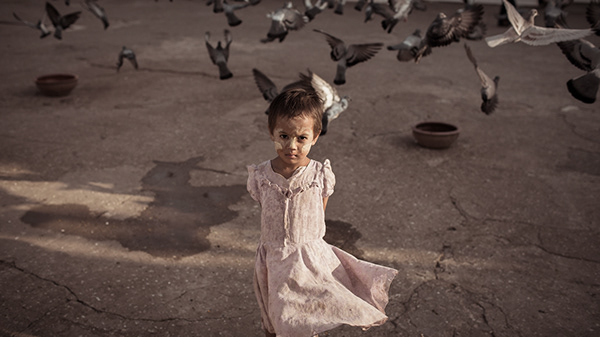 Young girl standing near pigeons in a sunlit courtyard