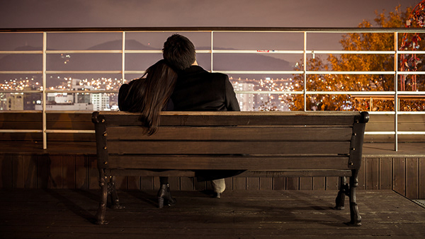 Person seated on a bench facing a waterfront railing