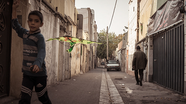 Person standing beside a wall in a narrow sunlit alley