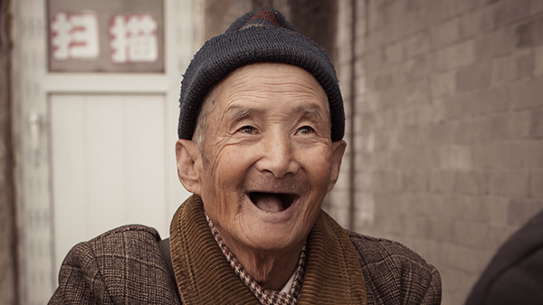 Older man wearing a dark cap and smiling