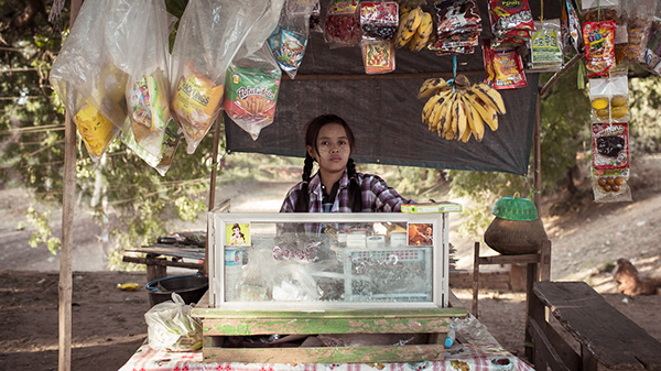 Vendor behind a stall displaying hanging fruit