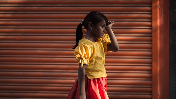 Girl in a yellow shirt standing in front of an orange shutter