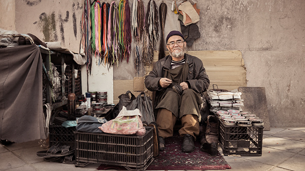 Older man sitting on crates beside a shop